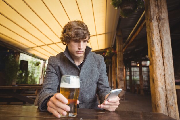 Mann, der Handy benutzt, während er ein Glas Bier hat