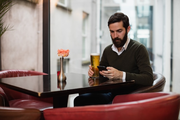 Mann, der Handy benutzt, während er ein Glas Bier hat