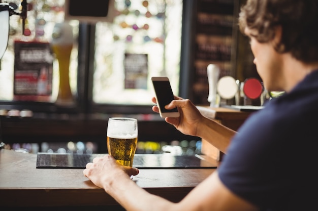 Mann, der Handy mit Glas Bier in der Hand benutzt