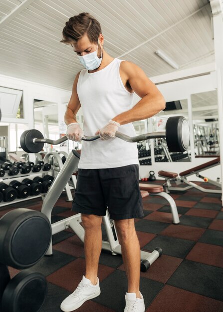 Mann, der herausarbeitet, während er medizinische Maske im Fitnessstudio trägt