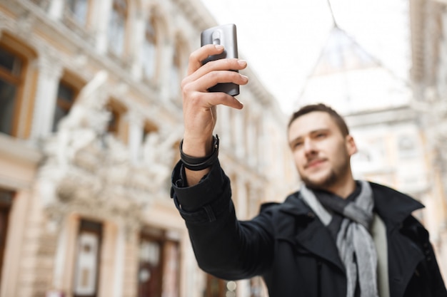 Mann, der herrliche Architektur am Telefon beim Gehen um Stadt schießt.