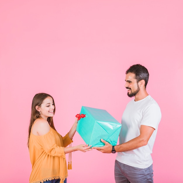 Mann, der ihrer Freundin über rosa Hintergrund Geschenk gibt