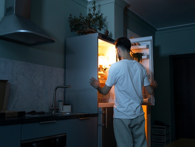 Kostenloses Foto mann, der im kühlschrank nach snacks sucht, mittlerer schuss