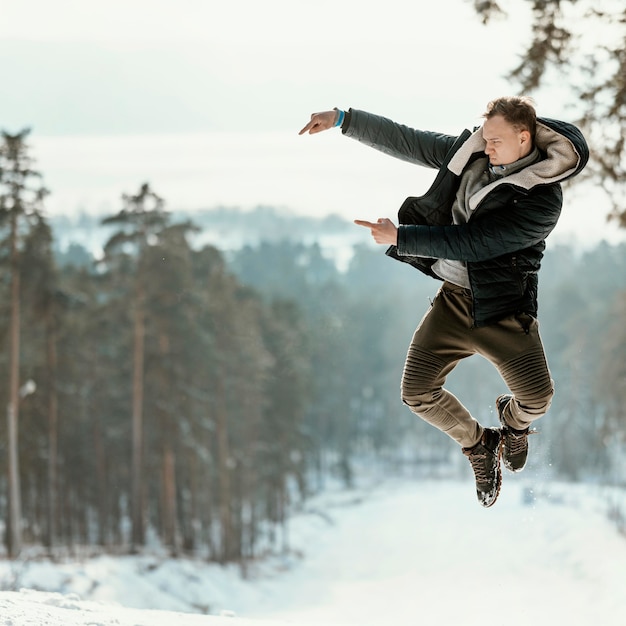 Mann, der im Winter im Freien in der Natur springt und auf Kopierraum zeigt