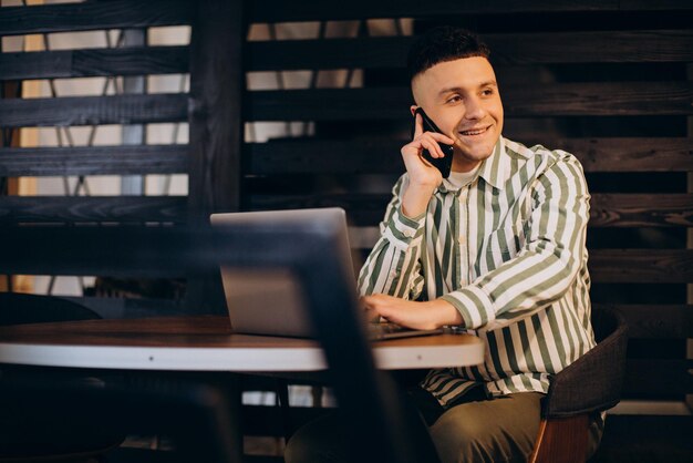 Mann, der in einem Café am Laptop arbeitet und telefoniert