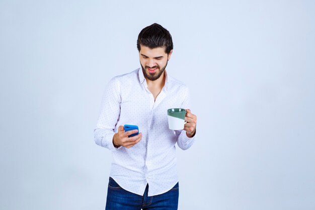 Mann, der in einer Hand eine Kaffeetasse hält und in der anderen auf sein Telefon schaut