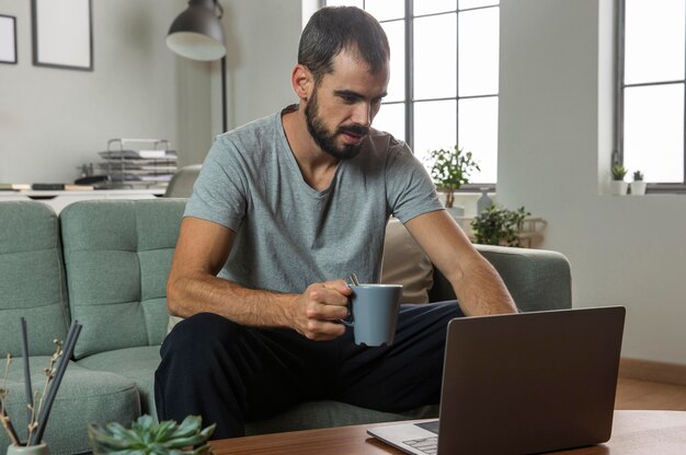 Mann, der Kaffee hat und von zu Hause auf Laptop arbeitet