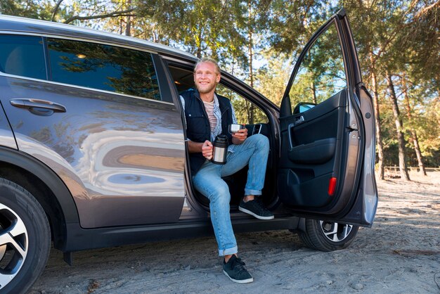 Mann, der Kaffee trinkt und in der langen Sicht des Autos sitzt