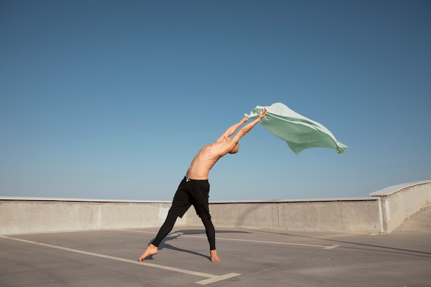 Mann, der künstlerischen Tanz auf einem Dach mit blauem Himmel aufführt