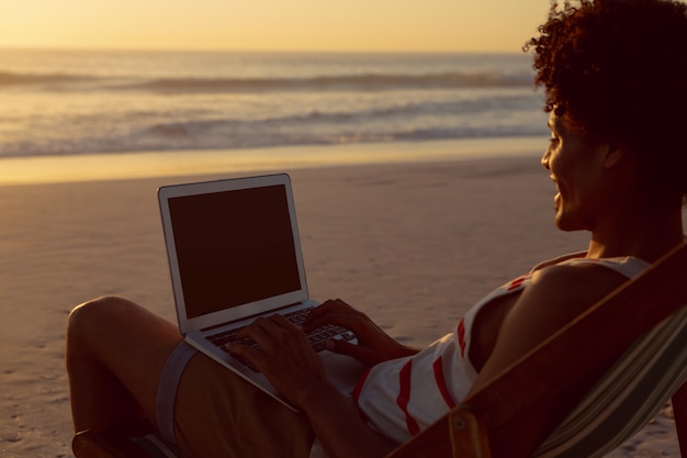 Mann, der Laptop bei der Entspannung in einem Strandstuhl auf dem Strand verwendet