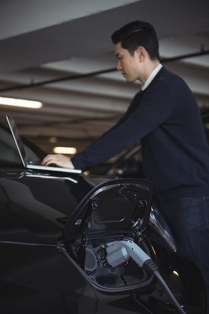 Mann, der Laptop beim Laden des Elektroautos verwendet