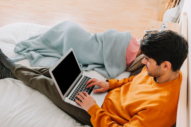 Mann, der Laptop nahe schlafender Frau durchstöbert