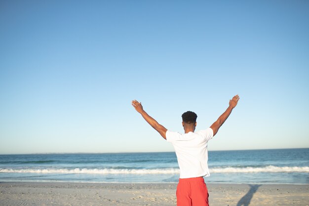Mann, der mit den Armen oben auf dem Strand steht