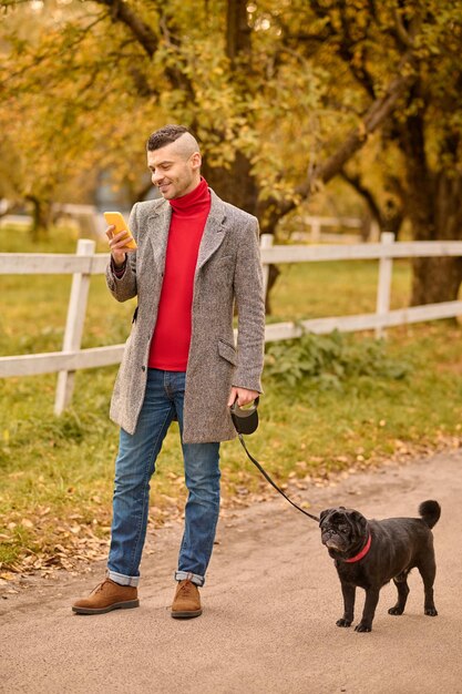 Mann, der mit einem Hund einen Morgenspaziergang macht und telefoniert