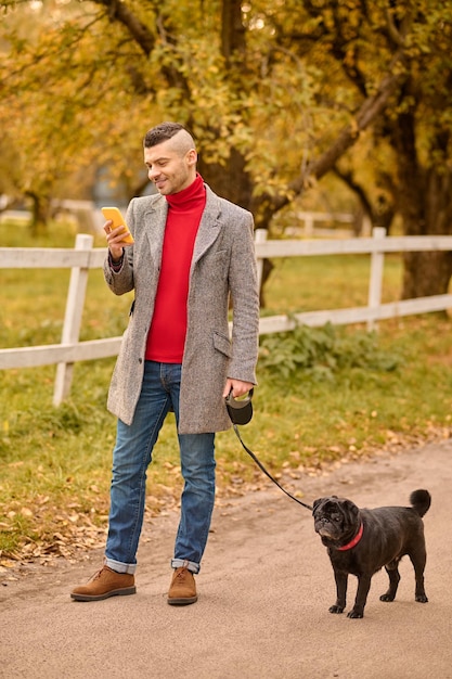 Mann, der mit einem Hund einen Morgenspaziergang macht und telefoniert