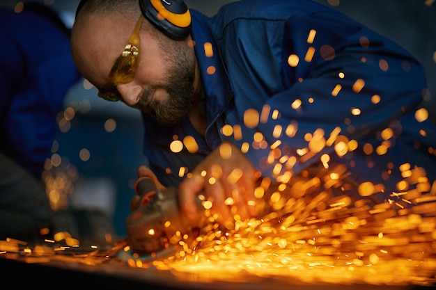 Mann, der mit Elektrostahlschneidemaschine in der Nähe von Funken arbeitet