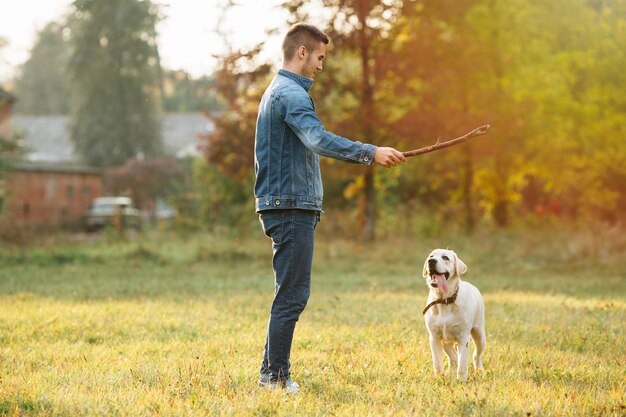 Mann, der mit Hund Labrador im Park bei Sonnenuntergang spielt