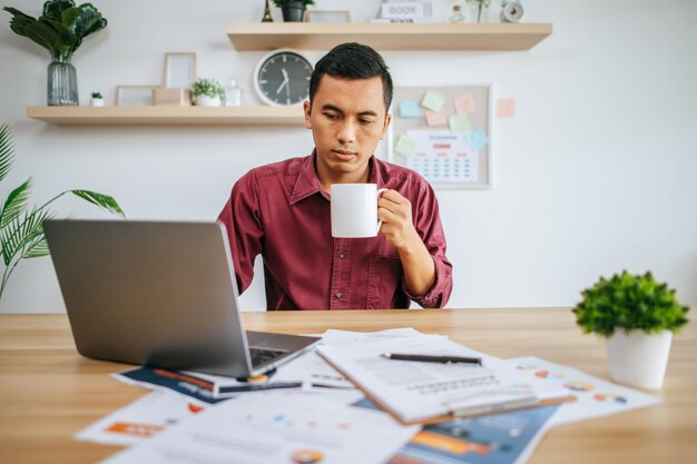 Mann, der mit Laptop arbeitet und Kaffeetasse hält