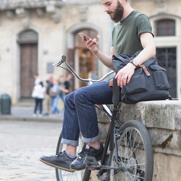 Mann, der mit seinem Fahrrad unter Verwendung des Mobiltelefons sitzt