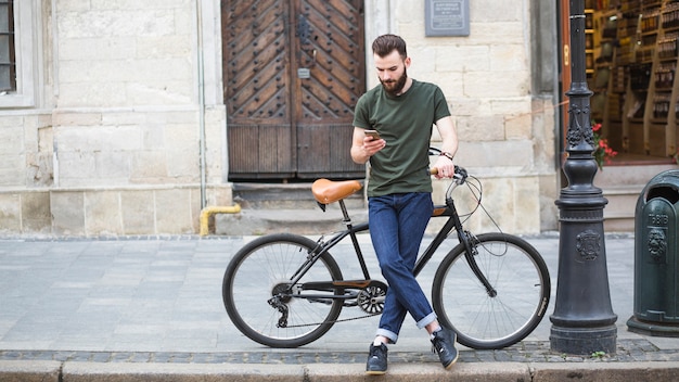 Mann, der mit seinem Fahrrad unter Verwendung des Smartphone steht