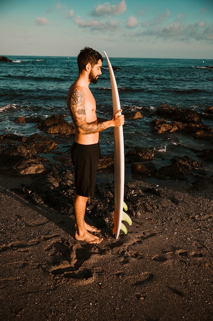 Mann, der mit Surfbrett auf Seeufer steht
