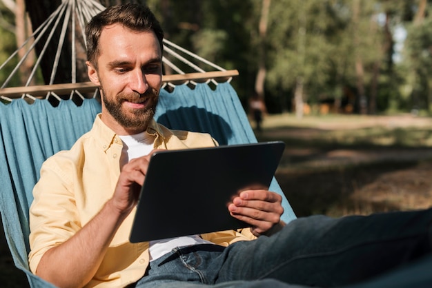 Kostenloses Foto mann, der mit tablette in der hängematte während des campings entspannt