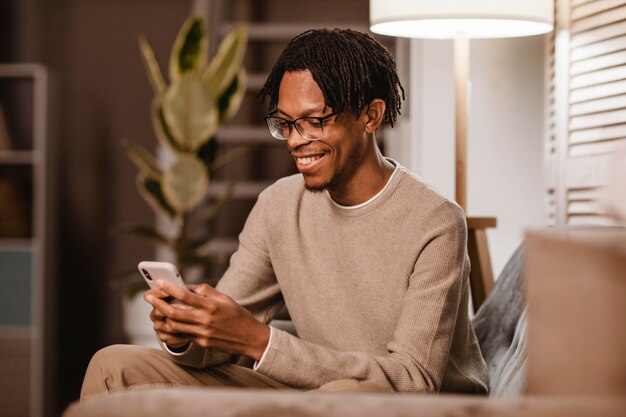 Mann, der modernes Smartphonegerät auf der Couch zu Hause verwendet