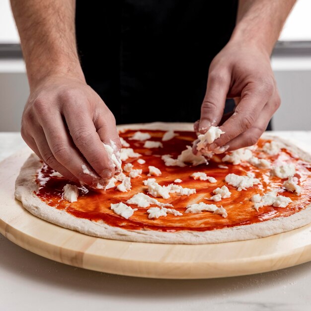 Mann, der Mozzarella auf Pizzateig setzt