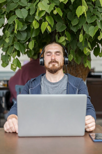 Mann, der Musik an einer Terrasse mit Laptop genießt