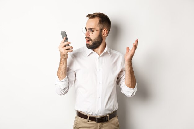 Mann, der nach dem Gespräch verwirrt auf Mobiltelefon schaut und verwirrt steht Kopierraum