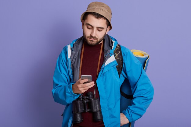 Mann, der Nachrichten für seine Familie von seinem Handy während des Wanderns sendet. Reisender in Hut und Jacke mit Handy-Anwendung