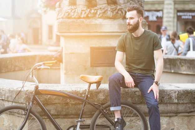 Kostenloses Foto mann, der nahe seinem fahrrad in der stadt sitzt