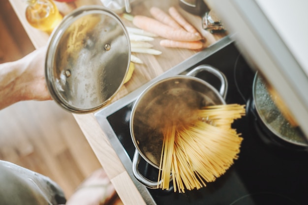 Mann, der Nudelspaghetti zu Hause in der Küche kocht. Hausmannskost oder italienisches Kochkonzept.