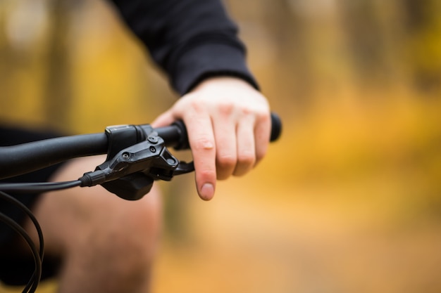 Mann, der sein Fahrrad durch einen Park auf einem Weg entlang einer bunten Schiene fährt, Nahaufnahme auf seinem Handrücken am Lenker