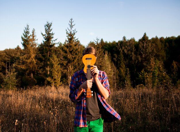 Mann, der sein Gesicht mit Ukulelegitarre bedeckt