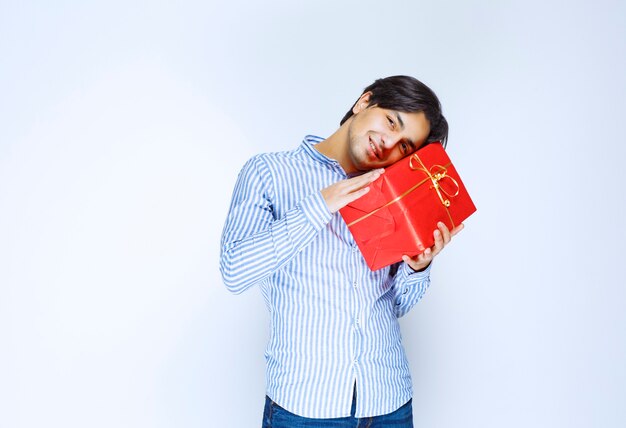 Mann, der seine wertvolle rote Geschenkbox umarmt. Foto in hoher Qualität