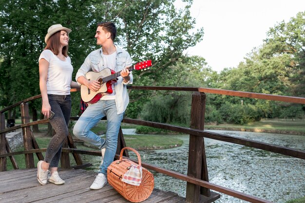 Mann, der seinem Mädchen auf einer Brücke Gitarre spielt