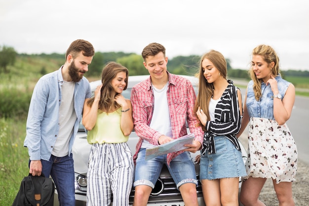 Mann, der seinen freunden karte nahe seinem auto zeigt