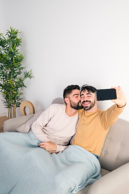 Mann, der Selbstporträt am Handy während sein Freundküssen nimmt