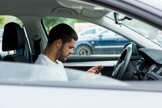 Mann, der Smartphone beim Sitzen im Auto verwendet