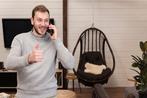 Mann, der Smartphone hält und zu Hause Daumen aufgibt