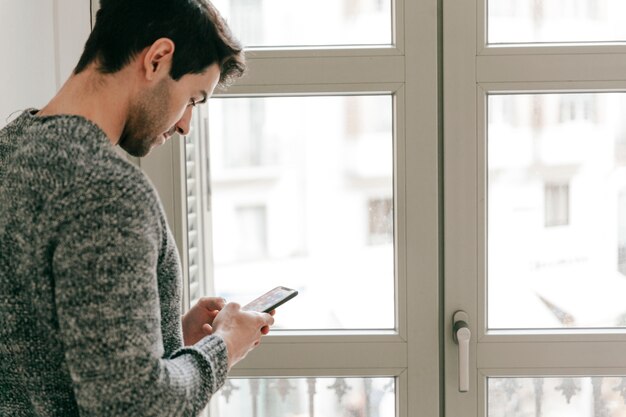 Mann, der Smartphone nahe Fenster verwendet