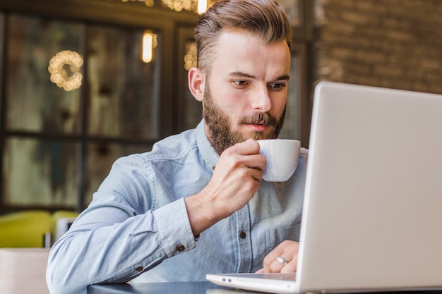 Mann, der trinkenden Tasse Kaffee des Laptops verwendet