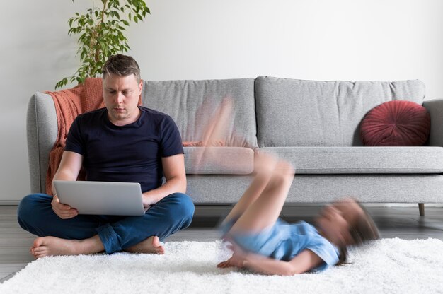 Mann, der versucht, von zu Hause aus am Laptop zu arbeiten, während ihre Kinder herumlaufen