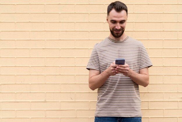 Mann, der vor Wand steht und sein Telefon benutzt