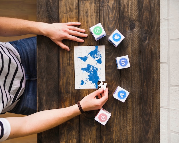 Mann, der Weltkartenpuzzle nahe Blöcken von Ikonen der sozialen Vernetzung löst