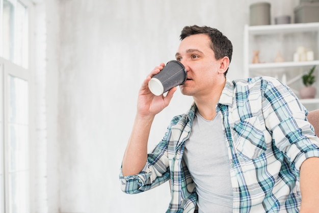 Kostenloses Foto mann, der zu hause vom cup auf stuhl trinkt