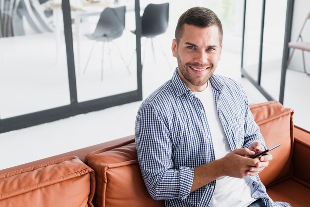 Mann des hohen Winkels zu Hause unter Verwendung des Mobiles