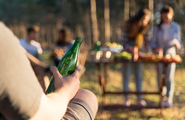 Mann draußen, der eine Flasche Bier mit Freunden am Tisch hält