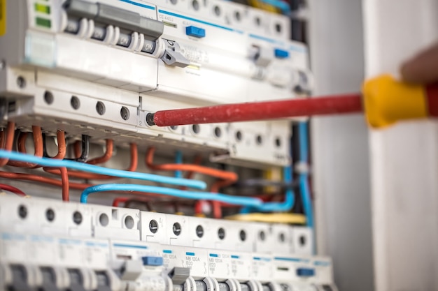 Mann, ein Elektrotechniker, der in einer Schalttafel mit Sicherungen arbeitet. Installation und Anschluss von elektrischen Geräten. Nahansicht.